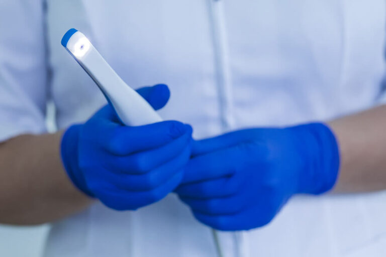 Image of a dental professional wearing blue gloves and holding an intraoral camera.